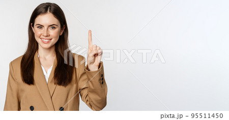 Portrait of corporate woman, saleswoman showing number one finger and smiling, standing in suit over white background Portrait of corporate woman, saleswoman showing number one finger and smiling, standing in suit over white background 95511450