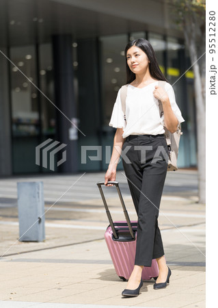 リュックを背負ってスーツケースを引いて歩くビジネスウーマン リュックを背負ってスーツケースを引いて歩くビジネスウーマン 95512280