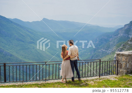 Happy couple tourists on background of Blue river running through green valley toward distant mountains. Beautiful mountains of Montenegro and the river Cievna Happy couple tourists on background of Blue river running through green valley toward distant mountains. Beautiful mountains of Montenegro and the river Cievna 95512778