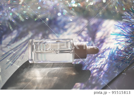 A bottle of serum with a pipette in tinsel in a Christmas theme in purple shades. 95515813