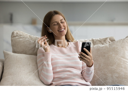 Beautiful woman holds smartphone listens favourite song through wireless earphones 95515946