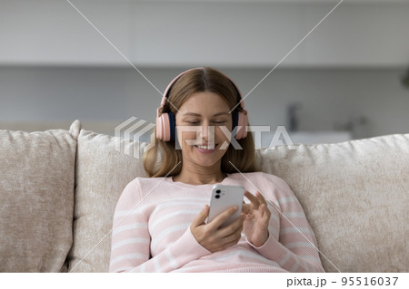 Woman in wireless headphones holds cellphone choose song in playlist 95516037