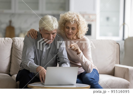 Couple sit on couch staring at laptop using ecommerce website Couple sit on couch staring at laptop using ecommerce website 95516095