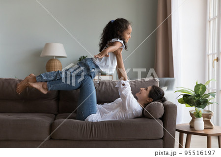 Indian mother lying on sofa plays with cute little daughter Indian mother lying on sofa plays with cute little daughter 95516197