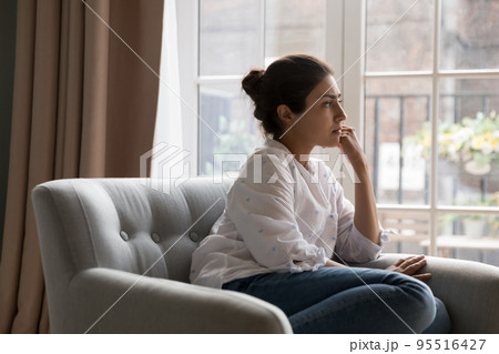 Sad Indian woman thinking sit on armchair and staring aside 95516427