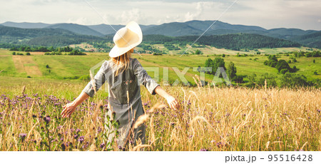 Woman in dress and hat staying at the green meadow in the mountain 95516428