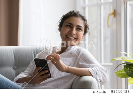 Peaceful Indian woman relaxing on cozy chair with smartphone Peaceful Indian woman relaxing on cozy chair with smartphone 95516488