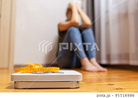 White scale and upset and sad woman with measuring tape on floor 95516986