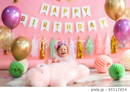 Laughing little girl sits near paper balls with teddy in holiday dress on pink birthday background Laughing little girl sits near paper balls with teddy in holiday dress on pink birthday background 95517854