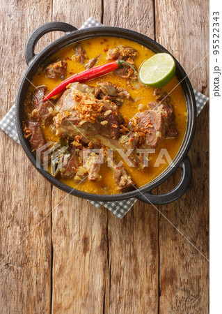 Spicy goat curry with coconut milk and spices close-up in a pan on the table. Vertical top view 95522343