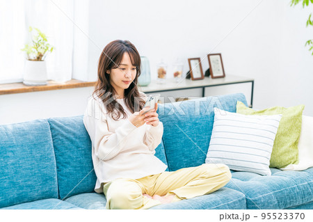 リビングでスマホを見る若い女性 95523370