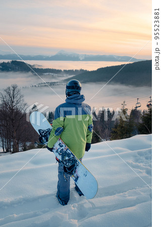 man snowboarder enjoying the view of sunset above the snowed mountains 95523881