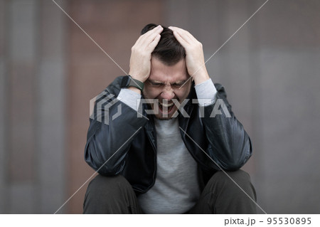 a man with a migraine attack sits clutching his head and screaming 95530895