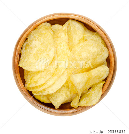 Salted potato chips, crisps in a wooden bowl. Thin slices of potato, deep fried in oil until crunchy. Served as a snack, side dish or appetizer. Close-up, from above, isolated over white, food photo. Salted potato chips, crisps in a wooden bowl. Thin slices of potato, deep fried in oil until crunchy. Served as a snack, side dish or appetizer. Close-up, from above, isolated over white, food photo. 95533835