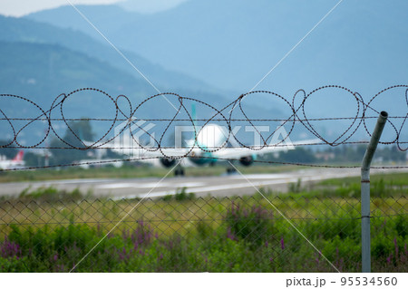 Barbed wire fence of airport against background of landing plane 95534560