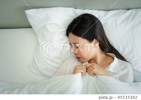 Unhappy exhausted woman closed eyes lying in bed cause of Headache, sore throat and tired, Concept of recuperation from illness, feeling unwell and healthcare. 95535302