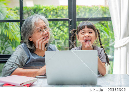 Asian Grandmother with her two grandchildren having fun and playing education games online with a computer notebook at home in the living room. Concept of online education and caring from parents. 95535306