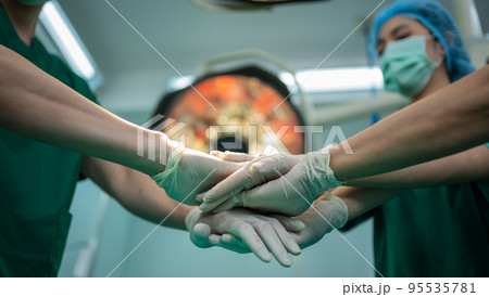 Asian surgeon and nurse with medical mask standing and join hand in operation theater at a hospital. Team of Professional surgeons. Healthcare, emergency medical service concept Asian surgeon and nurse with medical mask standing and join hand in operation theater at a hospital. Team of Professional surgeons. Healthcare, emergency medical service concept 95535781