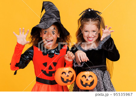 Happy children girls in witch costume and terrible makeup with pumpkin basket make scary gestures on Halloween  95535967