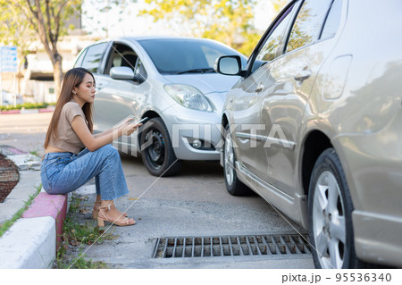 Woman drivers call insurance after a car accident before taking pictures and sending insurance. Online car accident insurance claim idea after submitting photos and evidence to an insurance company. 95536340