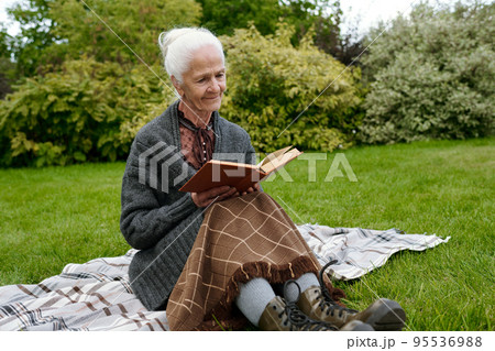 Senior woman in casualwear sitting on checkered woolen plaid and reading Senior woman in casualwear sitting on checkered woolen plaid and reading 95536988