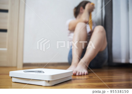 White scale and depression, upset and sad woman with measuring tape White scale and depression, upset and sad woman with measuring tape 95538150