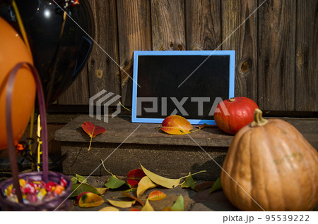 Selective focus. A blackboard with copy advertising space, next to pumpkins on a wooden threshold with fallen yellow and red leaves in autumn. Porch or backyard decoration. Halloween trick and treat 95539222