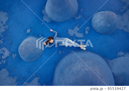 woman in blue jeans and a shirt is lying on a blue background on a sports field or in a park. a combination of colors, 95539427