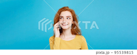 Lifestyle and Technology concept - Portrait of cheerful happy ginger red hair girl with joyful and exciting talking with friend by mobile phone. Isolated on Blue Pastel Background. Copy space. Lifestyle and Technology concept - Portrait of cheerful happy ginger red hair girl with joyful and exciting talking with friend by mobile phone. Isolated on Blue Pastel Background. Copy space. 95539815