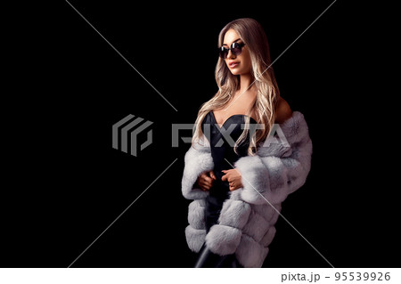Glamour blonde girl posing in luxurious fur coat and sunglasses while standing on black background 95539926