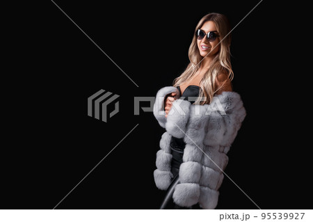 Attractive blonde girl in sunglasses posing on a black background in a fur coat. Commercial concept Attractive blonde girl in sunglasses posing on a black background in a fur coat. Commercial concept 95539927