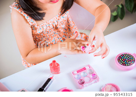 little girl making makeup dips brush into bottle to paints nails polish red nail varnish herself 95543315