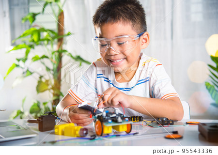 Asian kid boy plugging energy and signal cable to sensor chip with Arduino robot car 95543336