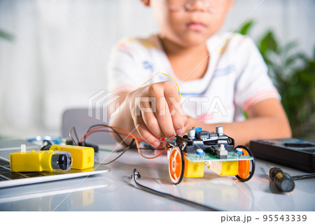 Asian kid boy plugging energy and signal cable to sensor chip with Arduino robot car 95543339