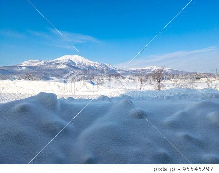 軒下に溜まった雪塊の向こうに雪原と山々 (北海道、俱知安町) 95545297