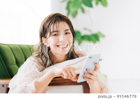 ソファに寝転がってスマホを持つ女性 95546779