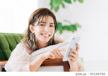 ソファに寝転がってスマホを持つ女性 95546780