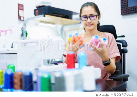 Embroidery, handicrafts, SME, family business Portrait of an Asian female designer picking up sewing threads for Design patterns using automatic embroidery machines according to customer orders 95547013
