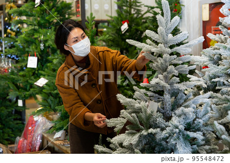 Woman in mask choosing christmas tree in store Woman in mask choosing christmas tree in store 95548472