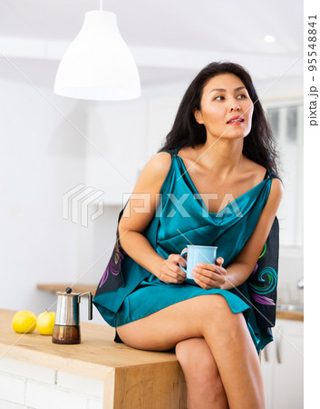Woman in nightie sitting on table at home and drinking tea Woman in nightie sitting on table at home and drinking tea 95548841