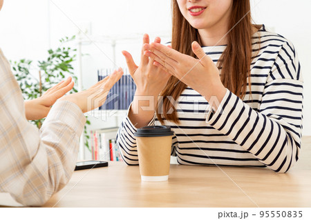 手を見ながらカフェで話す若い女性二人 95550835