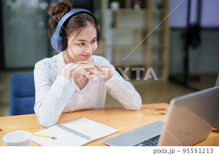 Portrait of a beautiful woman using a computer and earphone during a video conference Portrait of a beautiful woman using a computer and earphone during a video conference 95551213