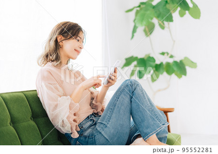 ソファーに座ってスマホを操作する若い女性 95552281