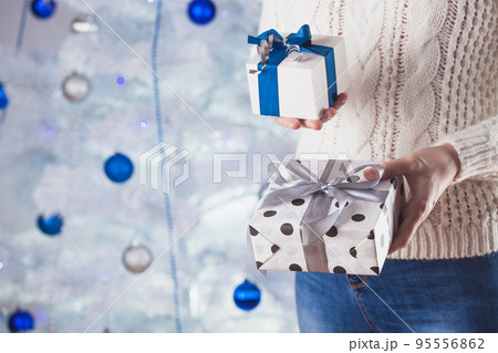 woman in white sweater and jeans in front of Christmas tree with present woman in white sweater and jeans in front of Christmas tree with present 95556862