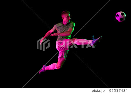 Young professional male football soccer player in motion isolated on dark background in neon light. Concept of sport, goals, competition, league, ad. 95557484
