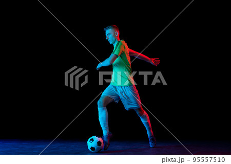 Goal. Young soccer, football player in motion and action with ball isolated on dark background in neon light. Concept of achievement, creativity, sport, energy, championship 95557510