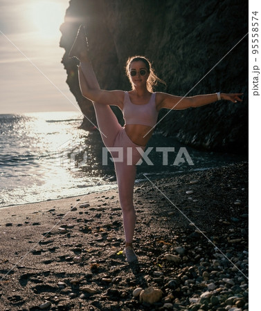 Young woman with black hair, fitness instructor in pink leggings and tops doing stretching and pilates on volcanic rocks near the sea on sunset. Female fitness yoga routine concept. Healthy lifestyle. Young woman with black hair, fitness instructor in pink leggings and tops doing stretching and pilates on volcanic rocks near the sea on sunset. Female fitness yoga routine concept. Healthy lifestyle. 95558574