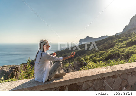 Profile of a woman doing yoga in the top of a cliff in the mountain. Woman meditates in yoga asana Padmasana 95558812