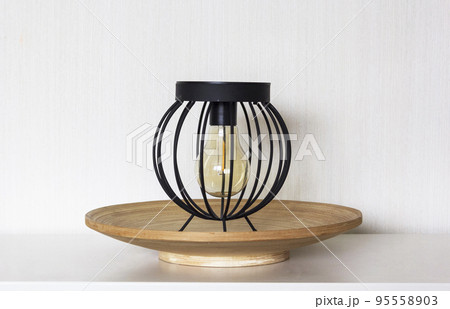 An antique lamp stands on a wooden stand on a white table. An antique lamp stands on a wooden stand on a white table. 95558903