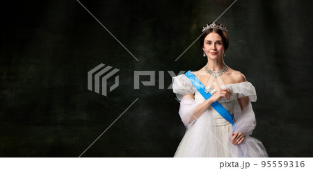 Young queen. Portrait of adorable girl in image of medieval royal person in renaissance style dress isolated on dark background. Comparison of eras, beauty, history, art 95559316